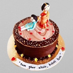 Funny Indian anniversary cake featuring a fondant bride dragging the groom with the Hindi text "Tum ghar chalo batati hun." Custom chocolate truffle design available for delivery in Hyderabad, Banjara Hills, and Jubilee Hills.