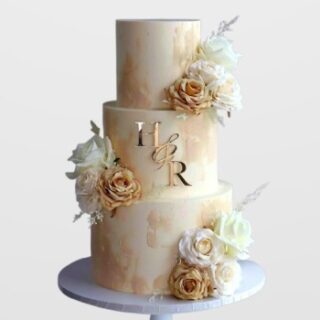 3-tier cream and gold watercolor engagement cake with floral bouquets and gold initials H & R. Custom rustic wedding cake delivery in Hyderabad, Banjara Hills, and Jubilee Hills.