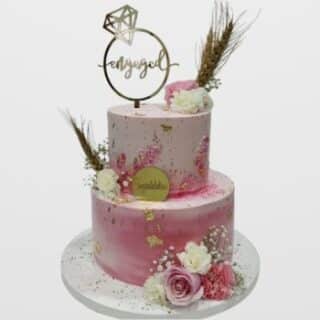 2-tier pink watercolor engagement cake with gold foil, dried wheat flowers, and gold "Engaged" ring topper. Boho custom cake delivery in Hyderabad, Madhapur, and Jubilee Hills.