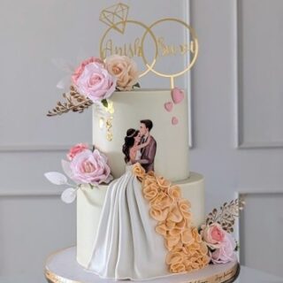 2-tier engagement cake with couple illustration, 3D fondant ruffle skirt, pink roses, and gold ring topper with names Anish and Suvi. Custom romantic wedding cake delivery in Hyderabad, Banjara Hills, and Jubilee Hills.